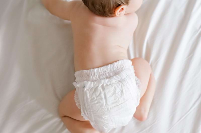 An infant wearing a diaper is crawling on the bed.