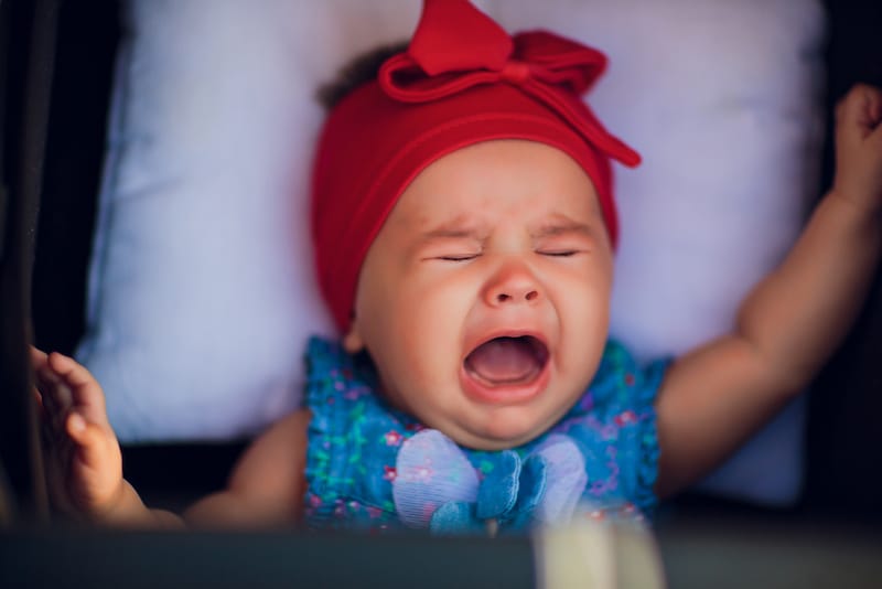 An infant girl is crying while she is being pushed in a baby stroller