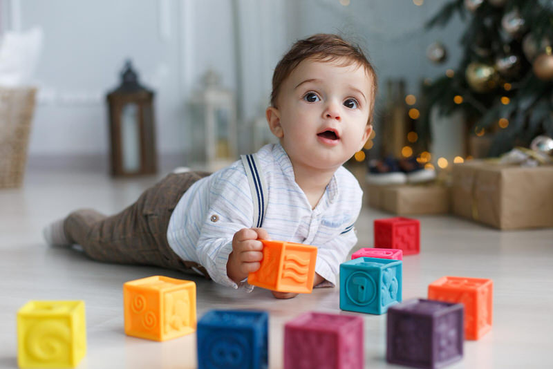 An infant boy is on his tummy playing with blocks in the living room