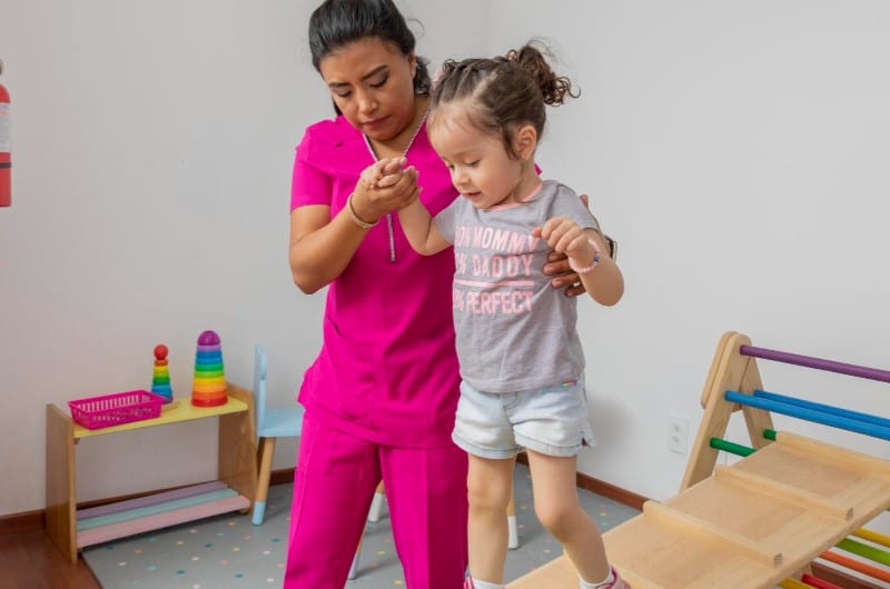A nurse is helping a small girl practice walking as part of her treatment plan for treating hypotonia. 