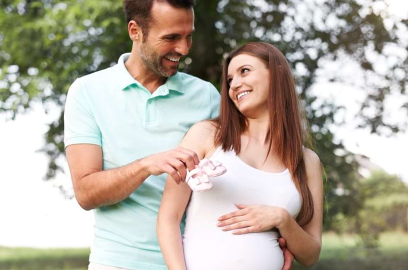 A couple feels really happy about welcoming their baby, and the father holds a pair of pink shoes. 
