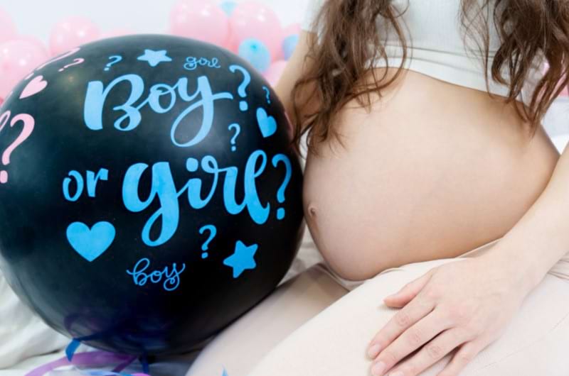 A pregnant woman is holding a balloon with a boy or girl written on it for her gender reveal party.