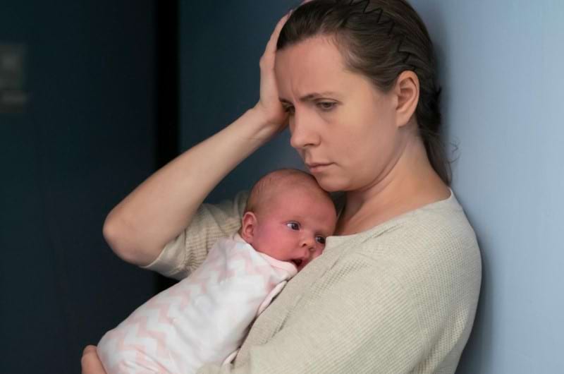 Mother suffering from postnatal depression holding baby in arms.