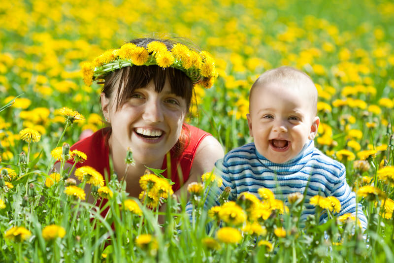 A young mom and her toddler son are having fun playing in a meadow of dandelions in their backyard