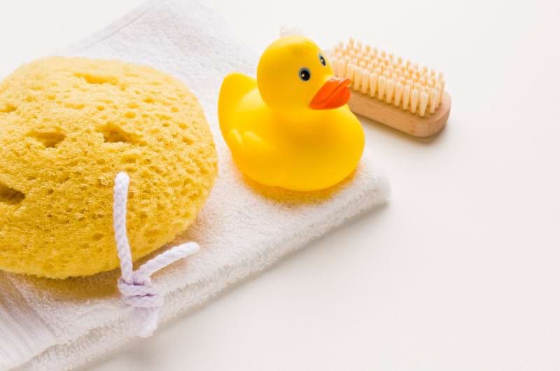 Bathing sponge, rubber duck, towel, and soft comb to use for baby bath.
