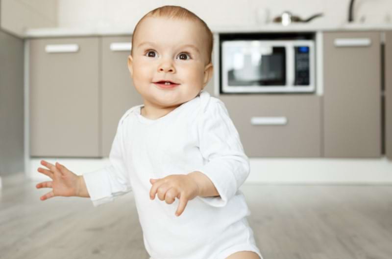 Cute baby dressed in cotton onesie playing in the kitchen.