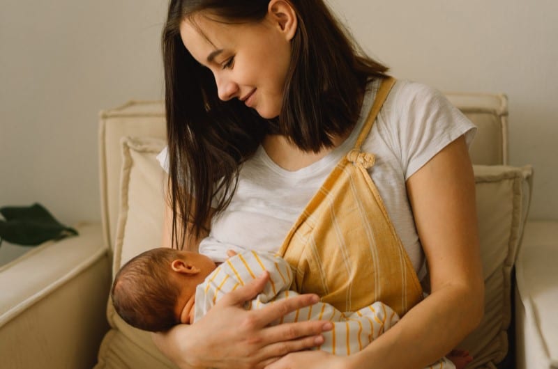 A newborn baby is breastfeeding, where the mother's hormones through breastmilk could be a possible cause of baby acne. 