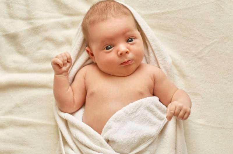 Newborn baby is wrapped in a towel after a breast milk bath.