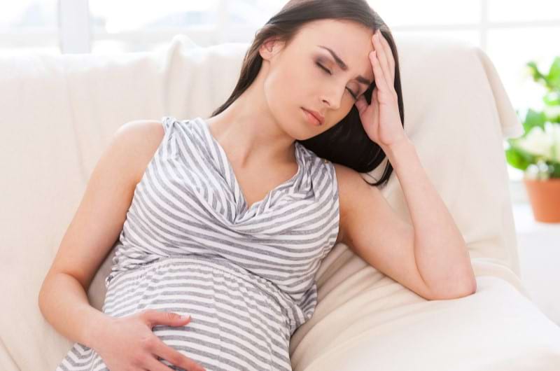 A young pregnant female sitting on the sofa is in pain due to her constipation issues.
