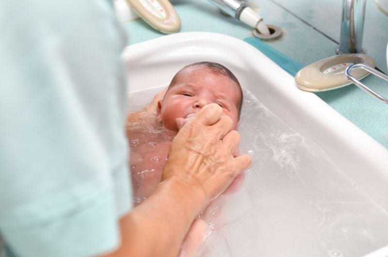 A woman giving bath to newborn and staying close to him all the time to avoid any accidents.