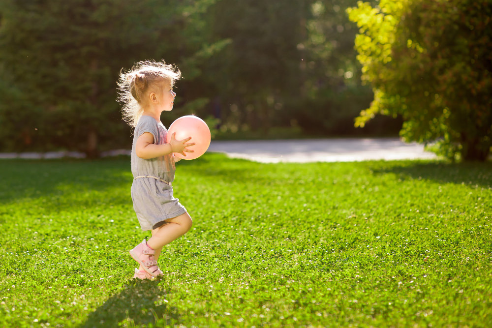 A toddler girl is playing with a ball outside on a sunny day