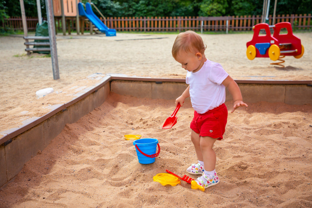 A toddler is playing in a sandbox at the park