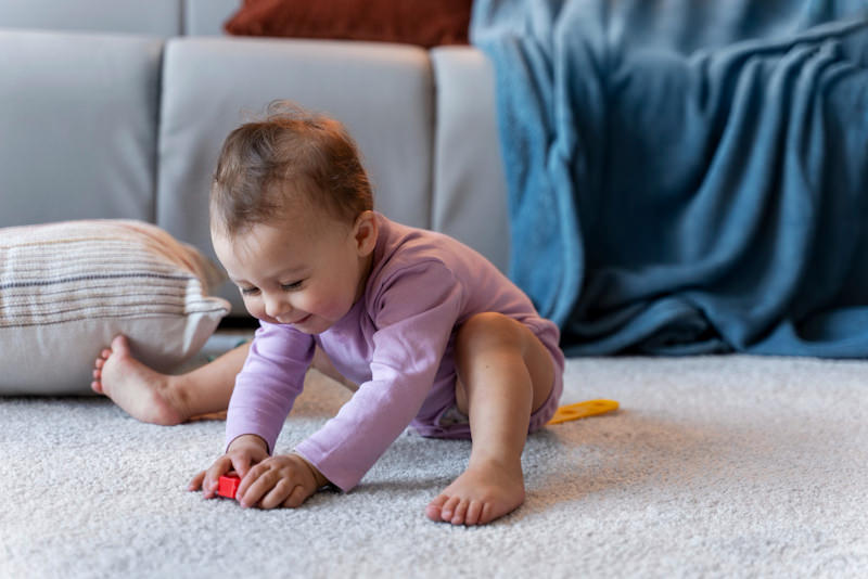 An infant baby girl is happily playing on the living room carpet