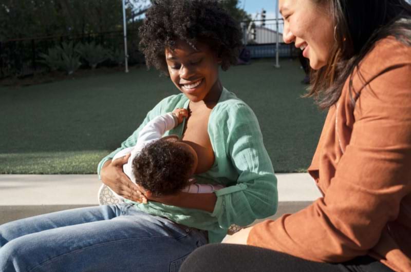 A mother is breastfeeding her baby in public with her female friend for support. 
