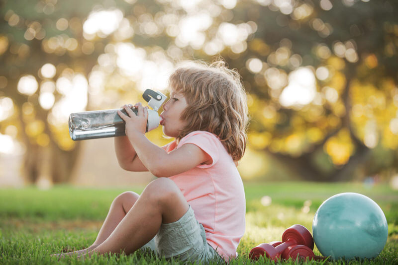A toddler is drinking water to stay hydrated while playing outside at the park on a sunny day
