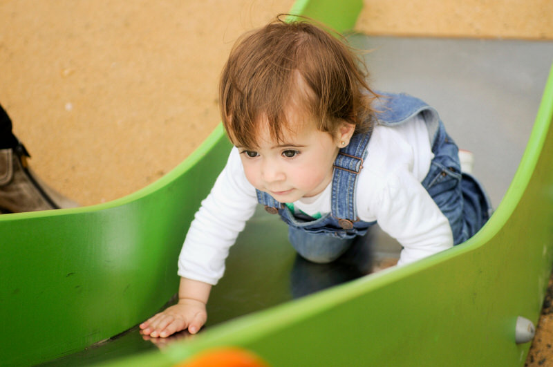A toddler girl is trying to go up the slide at the park