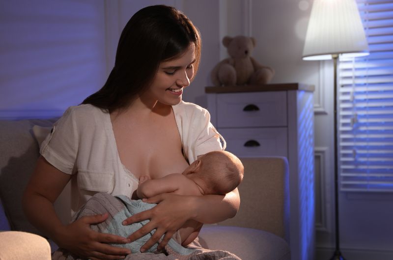 Mom is breastfeeding her newborn baby in the nursery before the baby goes to sleep at night
