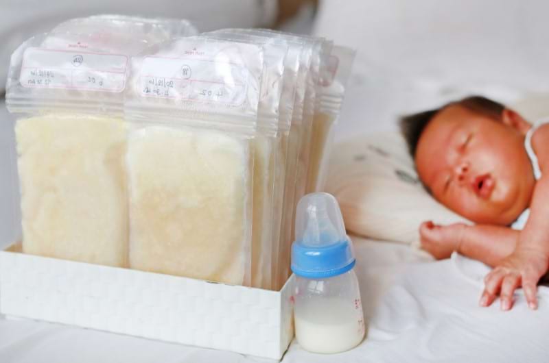 A baby is sleeping with frozen milk bags beside him that his mother uses to feed him when she's away working.
