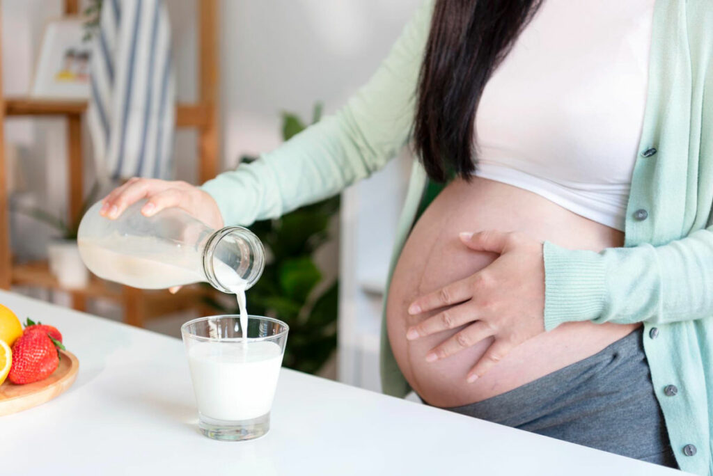 A pregnant woman is pouring herself a cup of milk to drink