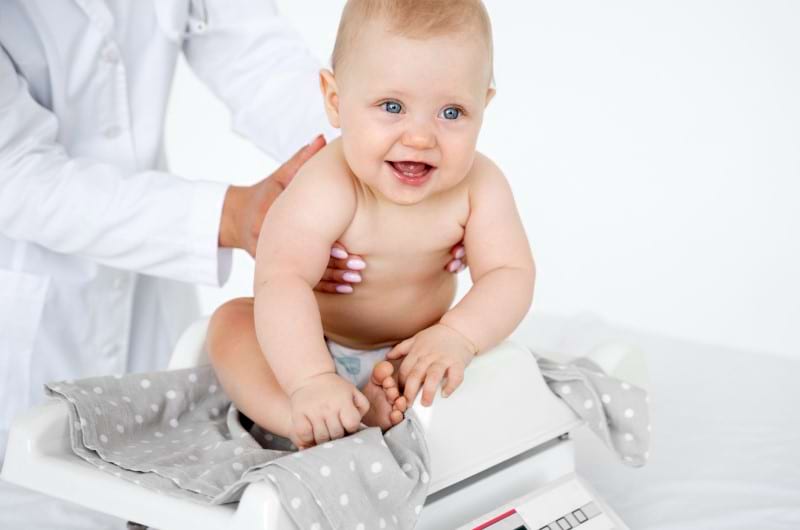 A pediatrician is weighting a little baby by placing him on the weighting scale. 