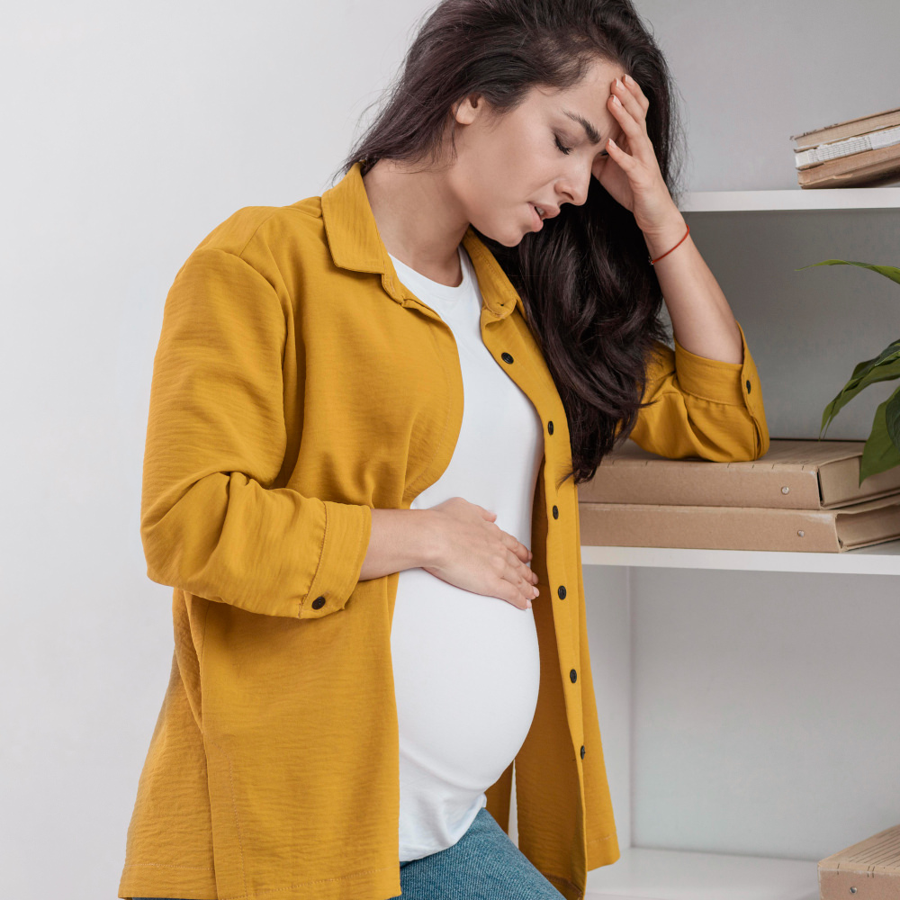 A pregnant woman is holding her belly and is looking noticeably unwell