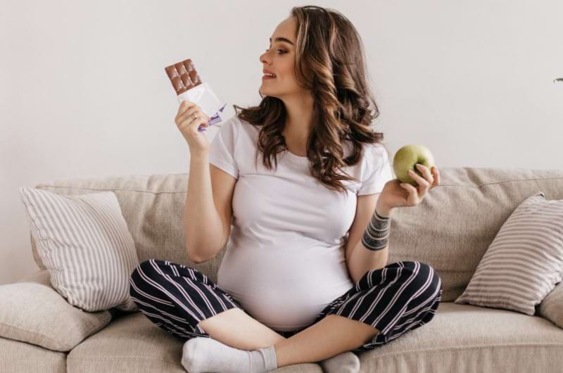 A pregnant lady is looking at chocolate more than fruits which can be bad for her health. 