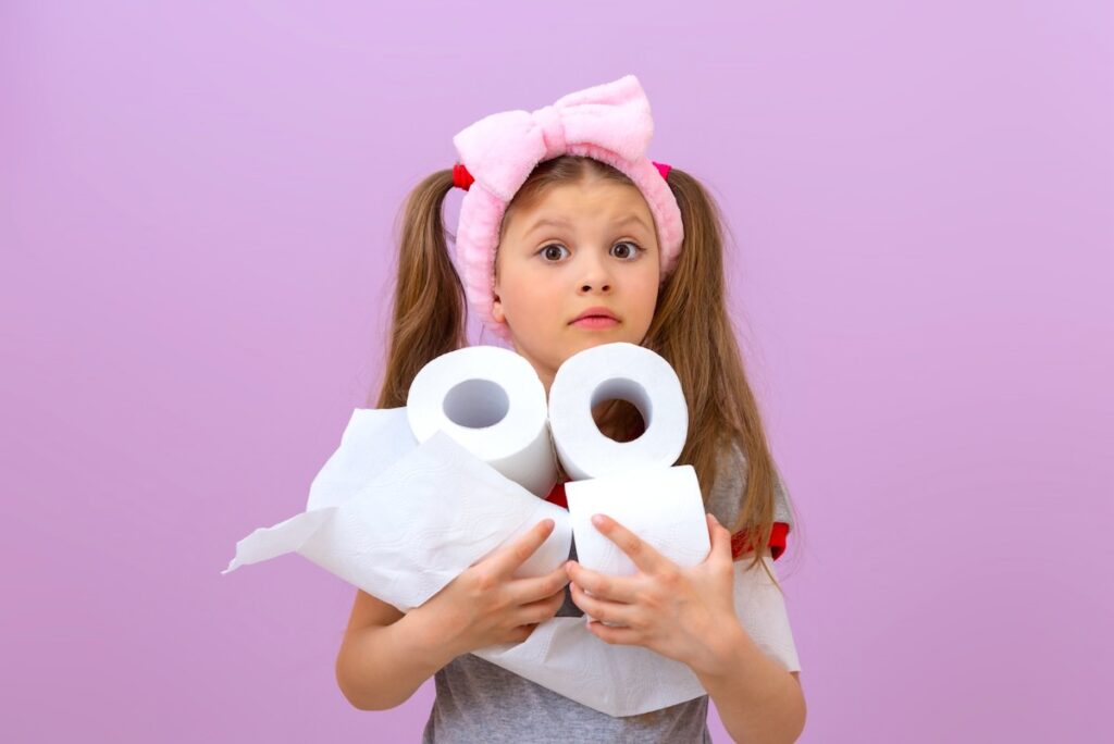 A young girl is holding several rolls of toilet paper